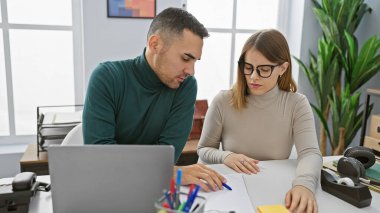 Parlak bir ofis ortamında çalışan bir adam ve kadın masadaki belgelere odaklanıyor..