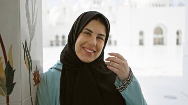 Abu Dabi 'de camide tesettürlü gülümseyen bir kadın Arap mimarisi ve İslam kültürü sergiliyor..