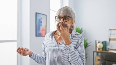 Modern ofis içinde akıllı telefon kullanan gri saçlı, olgun İspanyol bir kadın..