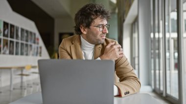 Paltolu dalgın sakallı bir adam modern bir ofis ortamında omuz ağrısı çekiyor..