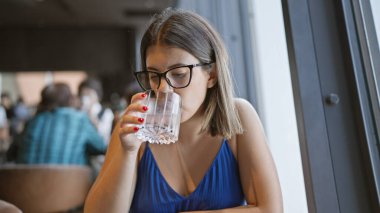 Tazeliğin tadını çıkar, güzel İspanyol kadın modern restoranda soğuk, temiz suyu yudumluyor - sağlıklı bir yaşam tarzı için mükemmel bir sıvı.