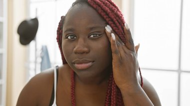 Örgülü güzel bir Afrikalı kadın düşünceli bir şekilde kapalı bir odada poz veriyor, moda ve stil anlayışı aktarıyor..