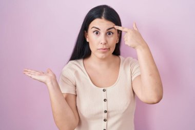 Pembe arka planda duran genç İspanyol kadının kafası karışmış ve avuç içi açık bir şekilde fotokopi alanı göstermesi ve alnını işaret etmesi canını sıkmış. Bunu bir düşün.. 