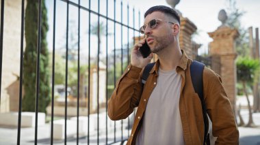 Şehir sokağında telefon kullanan güneş gözlüklü yakışıklı bir İspanyol.