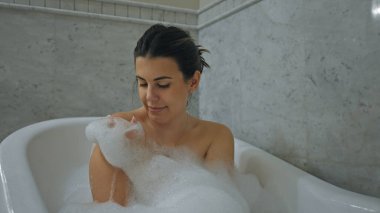 Genç yetişkin bir kadın, modern bir banyo ortamında huzur ve kişisel bakım göstererek rahatlatıcı bir banyonun keyfini çıkarıyor..
