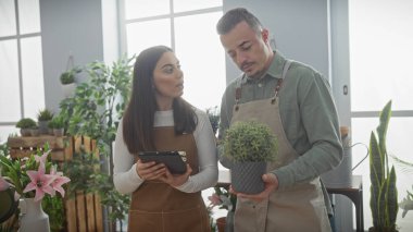 Önlüklü bir adam ve kadın, kapalı bir çiçekçide canlı çiçeklerin arasında tablet üzerinde tartışıyorlar..