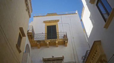 Gelibolu, Puglia, İtalya 'daki büyüleyici sokak manzarası balkonlu ve açık mavi gökyüzü olan eski binaları gösteriyor..