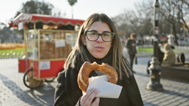 Genç bir kadın İstanbul caddesinde geleneksel bir Türk simit yiyor, hindi turizminin özünü somutlaştırıyor..