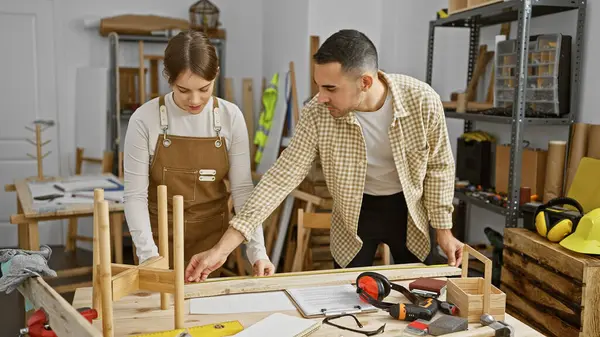 stock image A man and woman work together in a well-equipped carpentry workshop, assembling a wooden structure.