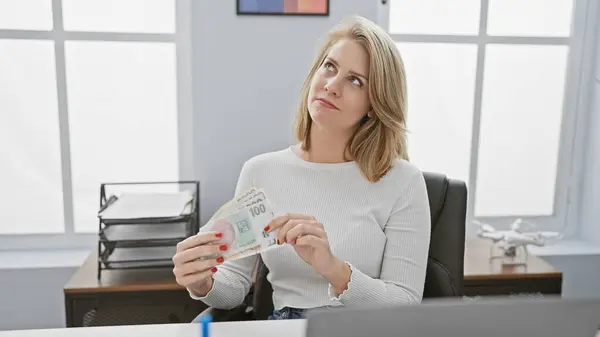 stock image A contemplative adult woman examines czech korunas in a modern office setting, suggesting financial work.