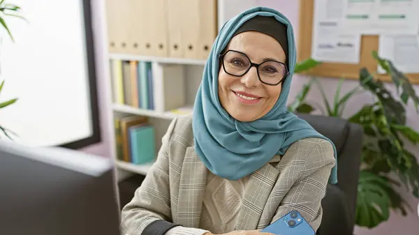 stock image Smiling woman in hijab with glasses working in a modern office environment.