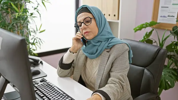 stock image Professional middle-aged woman in hijab speaking on phone in modern office setting