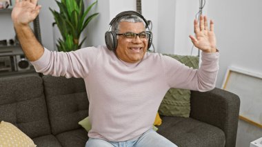 Gri saçlı mutlu bir orta yaşlı adam müzik dinler ve evinde neşeyle dans eder..