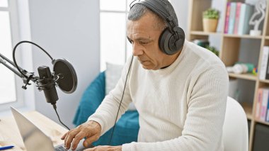 Telsiz stüdyosunda dizüstü bilgisayar kullanan, kulaklıklı, olgun bir İspanyol..