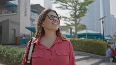 Dubai 'de, marina kulelerinin yanındaki lüks deniz manzaralı, gülümseyen, genç, İspanyol, esmer kadın.