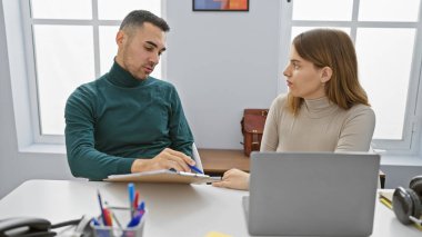 A man and woman coworking in a bright modern office discuss over a document, symbolizing teamwork and partnership. clipart