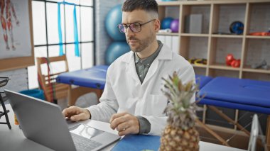 Modern fizyoterapi kliniğinde rehabilitasyon ekipmanlarıyla çalışan gözlüklü İspanyol bir adam..