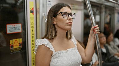Güzel İspanyol kadın, gözlüklü, metro geçişinde bekliyor, şehir şehrinin boş yeraltı demiryolundaki modern esmer yolcu portresi, toplu taşıma araçlarıyla seyahat ediyor.