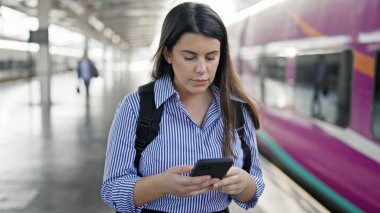 Tren istasyonunda akıllı telefon kullanarak demiryolunda yürüyen genç ve güzel bir İspanyol kadın.