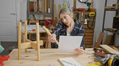 Sarışın bir kadın dağınık bir marangoz atölyesinde mobilya montajı yaparken planlarını inceliyor.