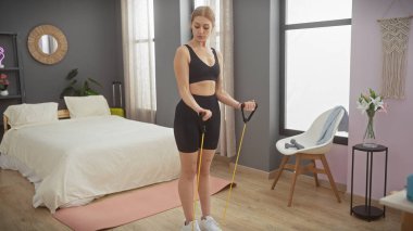 Modern yatak odası ortamında direnç bantlarıyla egzersiz yapan genç bir kadın sağlıklı bir yaşam tarzını somutlaştırıyor..
