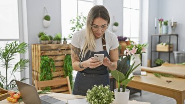 Çiçekçide akıllı telefon kullanan genç bir kadın.