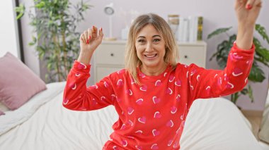 Kırmızı pijamalı, neşeli, sarışın, orta yaşlı bir kadın. Kalp desenli. Parlak bir yatak odasında kollarını uzatıyordu..