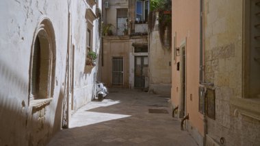 Lecce 'de sessiz bir ara sokak, eski binalarla dolu bir puglia ve güneşli bir günde bu İtalyan kasabasının pitoresk, tarihi cazibesini temsil eden park etmiş bir scooter..