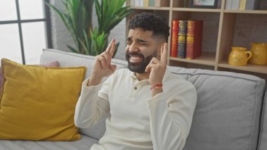 Gri bir kanepede otururken şans dilemek için evde oturan kederli, genç bir İspanyol..