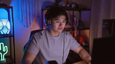 Odaklanmış genç Asyalı bir adam geceleri karanlık bir odada neon ışıklarla oynuyor..