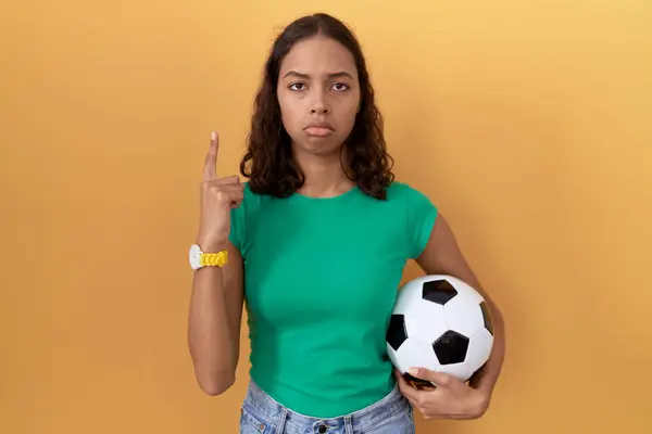 stock image Young hispanic woman holding ball pointing up looking sad and upset, indicating direction with fingers, unhappy and depressed. 