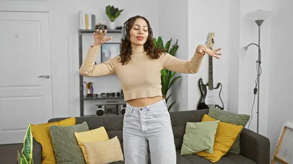 A joyful young woman dances alone in a modern living room, surrounded by cozy decor and a guitar in the background.