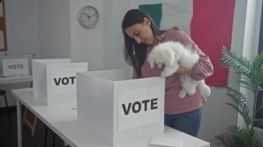Meksika 'da bir üniversitede arka planda bayraklı bir seçim odasında bichon köpeğini tutan gülümseyen İspanyol bir kadın..