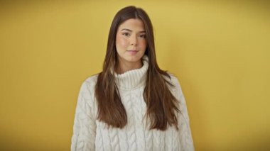 Neşeli genç İspanyol kadın gururla bir şeyler sergiliyor, avuç içi ile el kol hareketi yapıyor ve geniş bir şekilde gülümsüyor. Sarı izole bir arka planda duruyor, şirin bir kazak giyiyor.!