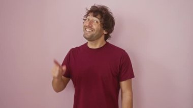 Neşeli İspanyol bir adam, tişört giyiyor, bir numaralı başarı fikrini işaret etmek için muzaffer bir şekilde parmağını kaldırıyor. Pembe bir arka plana karşı tek başına duruyor. Zeka ve coşku saçıyor..