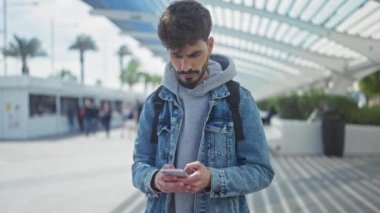 Odaklanmış, sakallı, şehir caddesinde akıllı telefon kullanan, gündelik ve şehir tarzı İspanyol bir adam.