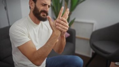 Beyaz tişörtlü yakışıklı, orta yaşlı bir adam ellerinde ve parmaklarında ağrılı eklem iltihabıyla uğraşıyor. Rahatsızlık yayıldıkça, kapalı alan terapileri ya da tıbbı düşünüyor..