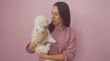 Mutlu genç bir kadın pembe izole edilmiş arka planda bichon köpeğini sevgiyle tutuyor..