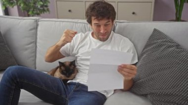 Beyaz gömlekli ve kotlu İspanyol bir adam. Gri bir kanepede, siyam kedisi ile neşeli, meraklı ve rahat hissediyor..