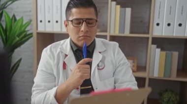 Laboratuvar önlüklü düşünceli bir İspanyol iyi organize edilmiş bir klinik odasındaki panoyu inceliyor..