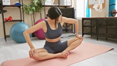 Rehabilitasyon kliniğinde yoga yapan genç bir kadın kapalı bir ortamda spor ve sağlık hizmetleri sunuyor.