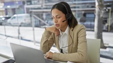 Modern bir ofis ortamında, muhtemelen boynu ağrıyan, kulaklık takan profesyonel bir İspanyol kadın acı çekiyor..
