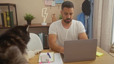 Evde dizüstü bilgisayarı üzerinde çalışan genç bir İspanyol adam yanında nazik köpeğiyle rahat bir oturma odasında hazırlanıyor.