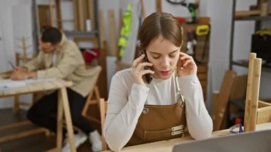 Bir kadın telefonla konuşuyor ve bir adam marangozluk atölyesinde çizim yapıyor, ikisi de görevlerine odaklanmış..