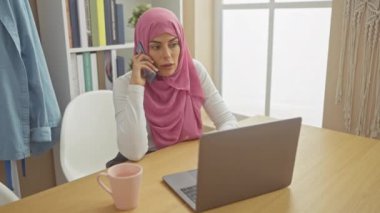 Dairesinde telefondayken kredi kartı tutan tesettürlü endişeli bir kadın..