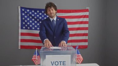 Takım elbiseli gülümseyen bir adam, arka planda Amerikan bayrağı olan Amerikan seçim kabininde oy kullanıyor..