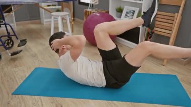 Odaklanmış bir adam içeride mavi bir paspas üzerinde spor yapıyor..