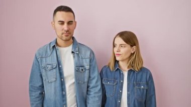 Kesin sesinizi! Güzel bir çift, pembe yalıtılmış arka planda kot gömleklerle duruyorlar, parmakları dudaklarına kadar sessiz ve gizli bir jest yapıyorlar. tutkulu bir ilişki sessizce gizlenir..