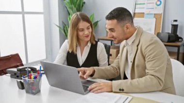 İş arkadaşları modern bir ofiste, neşeli bir kadın ve dizüstü bilgisayar kullanan odaklanmış bir adamla çalışmayı tartışıyor..