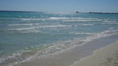 Sakin sahil sahnesi, hafif dalgalar porto sezeryan kıyılarını sarıyor, puglia, İtalya, berrak mavi bir gökyüzünün altında.
